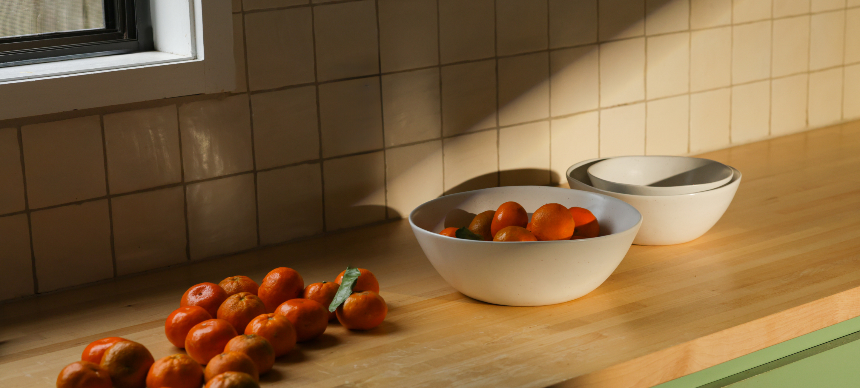 White bowls with oranges on a sunlit wooden kitchen counter.