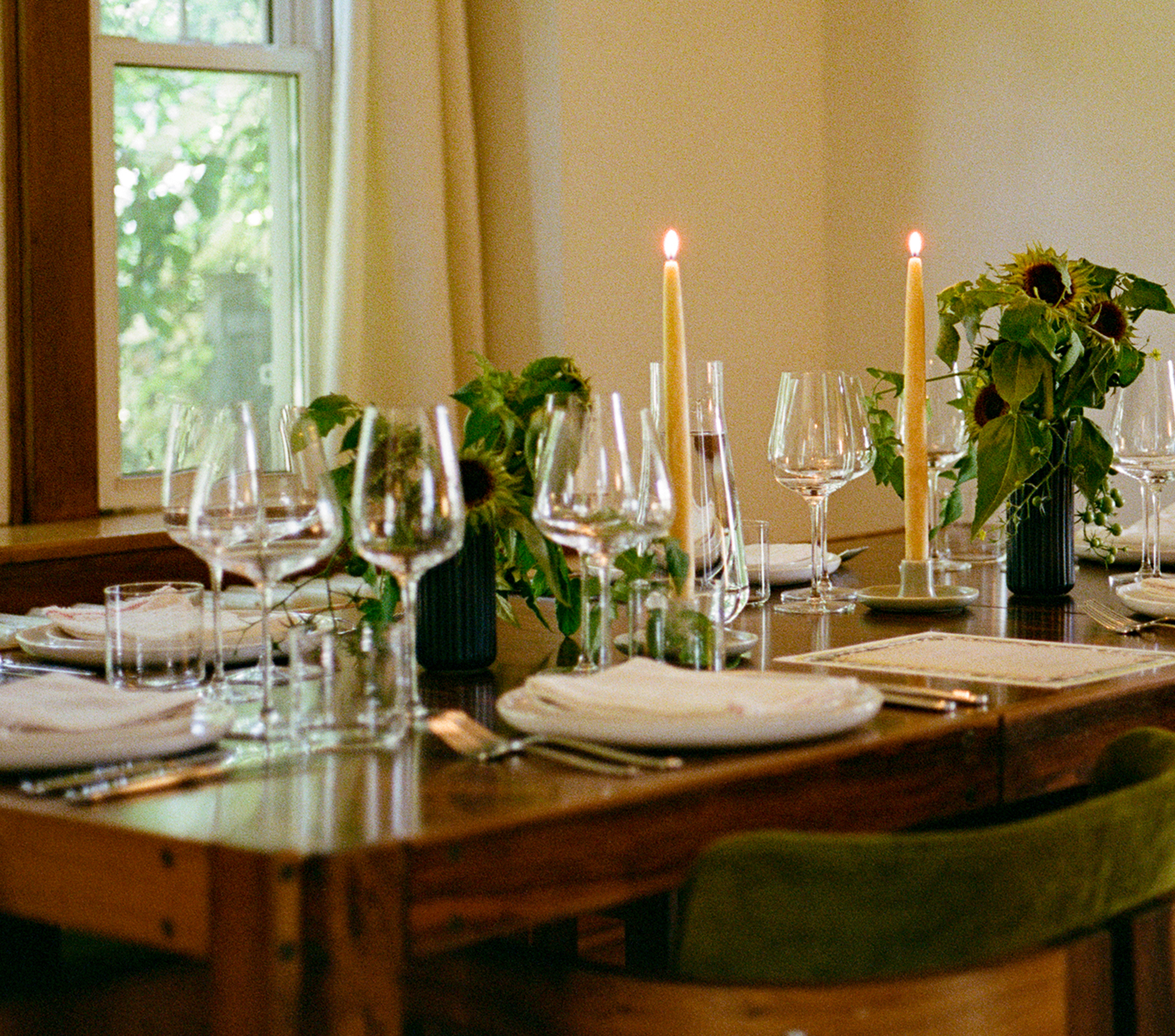 Elegant dining table set with candles, glassware, and green floral arrangements.