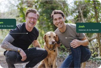 Two smiling people with a dog in a park setting.