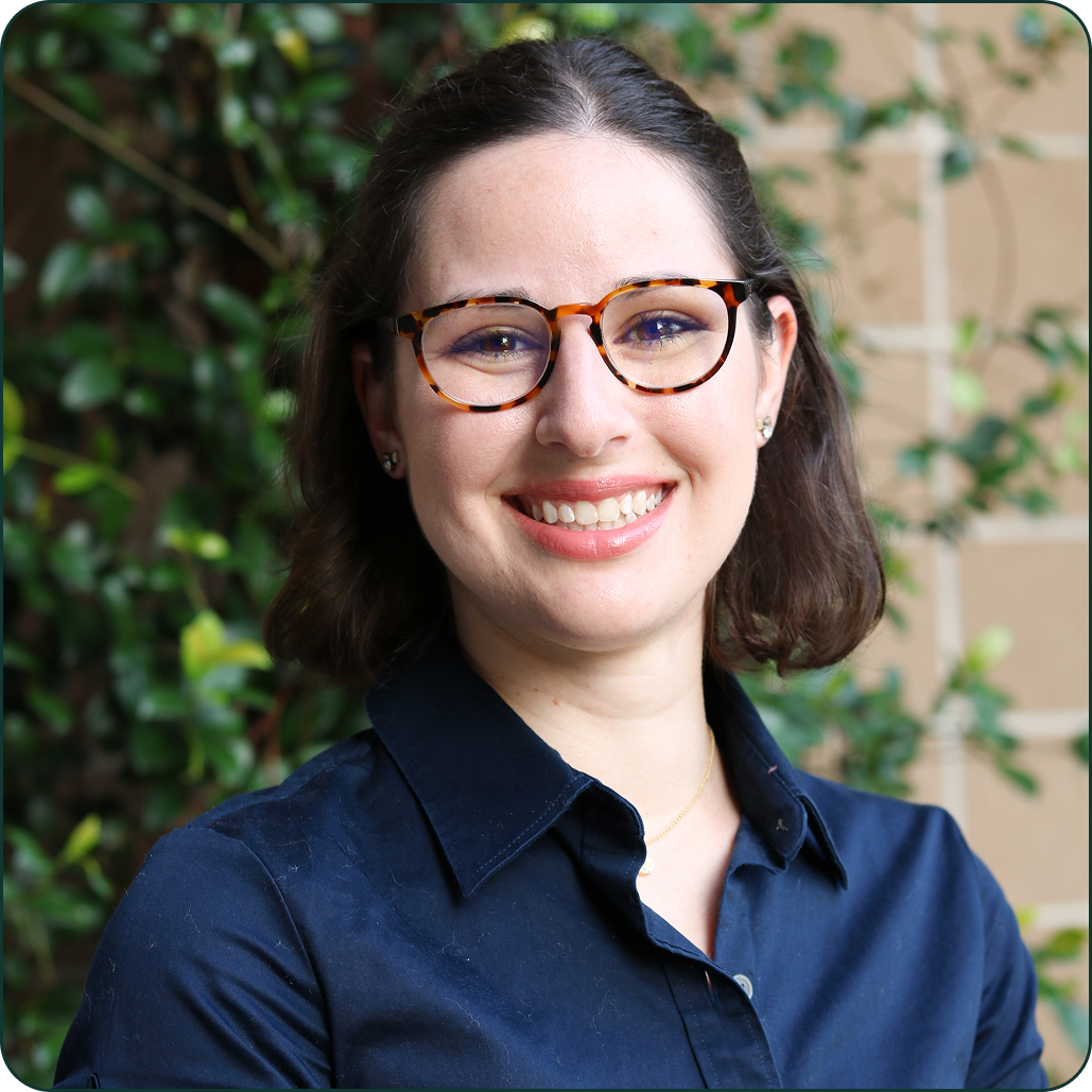 Person smiling with glasses, wearing a navy shirt, in front of green plants.