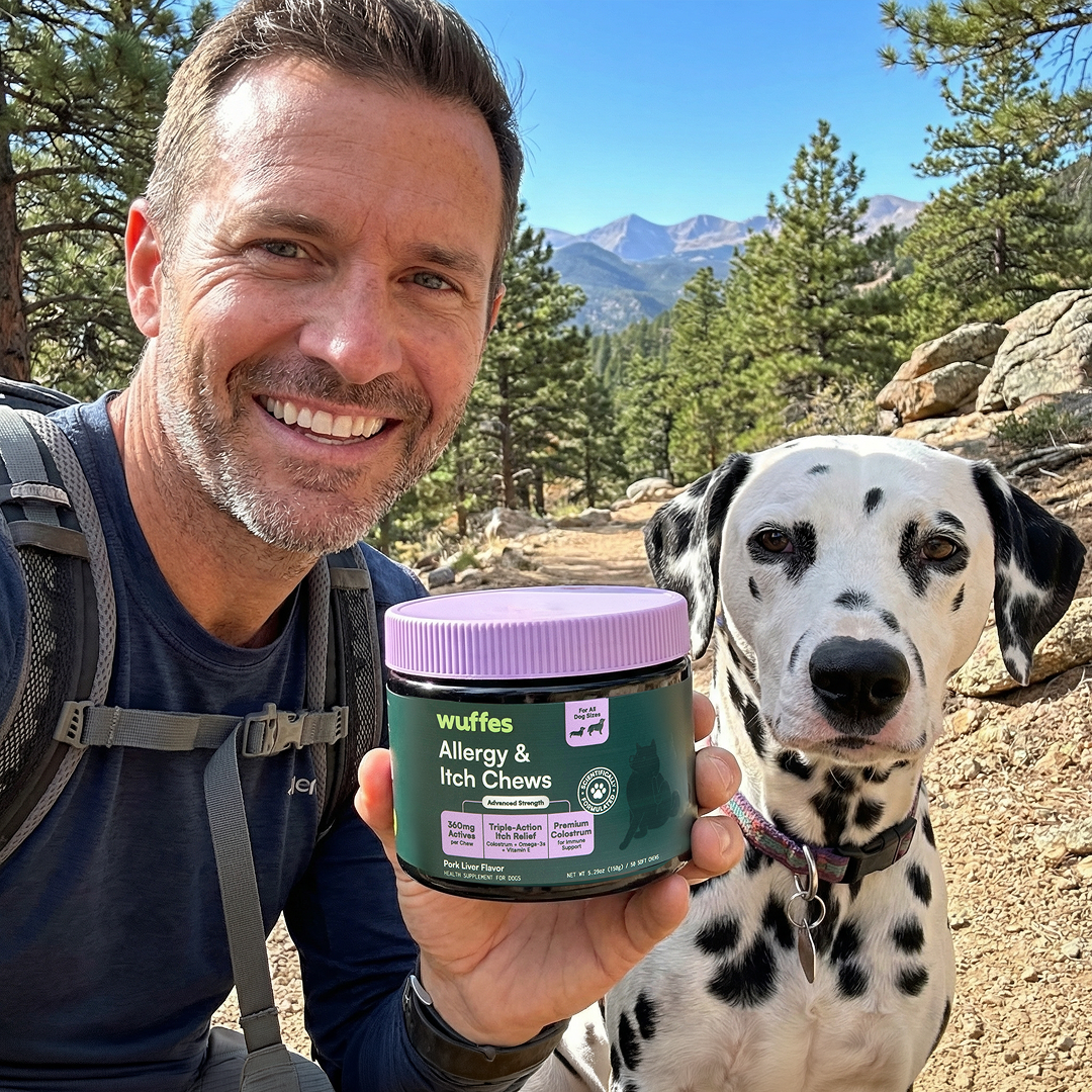 A smiling man holds a jar of Wuffes dog chews while hiking with his dalmatian.