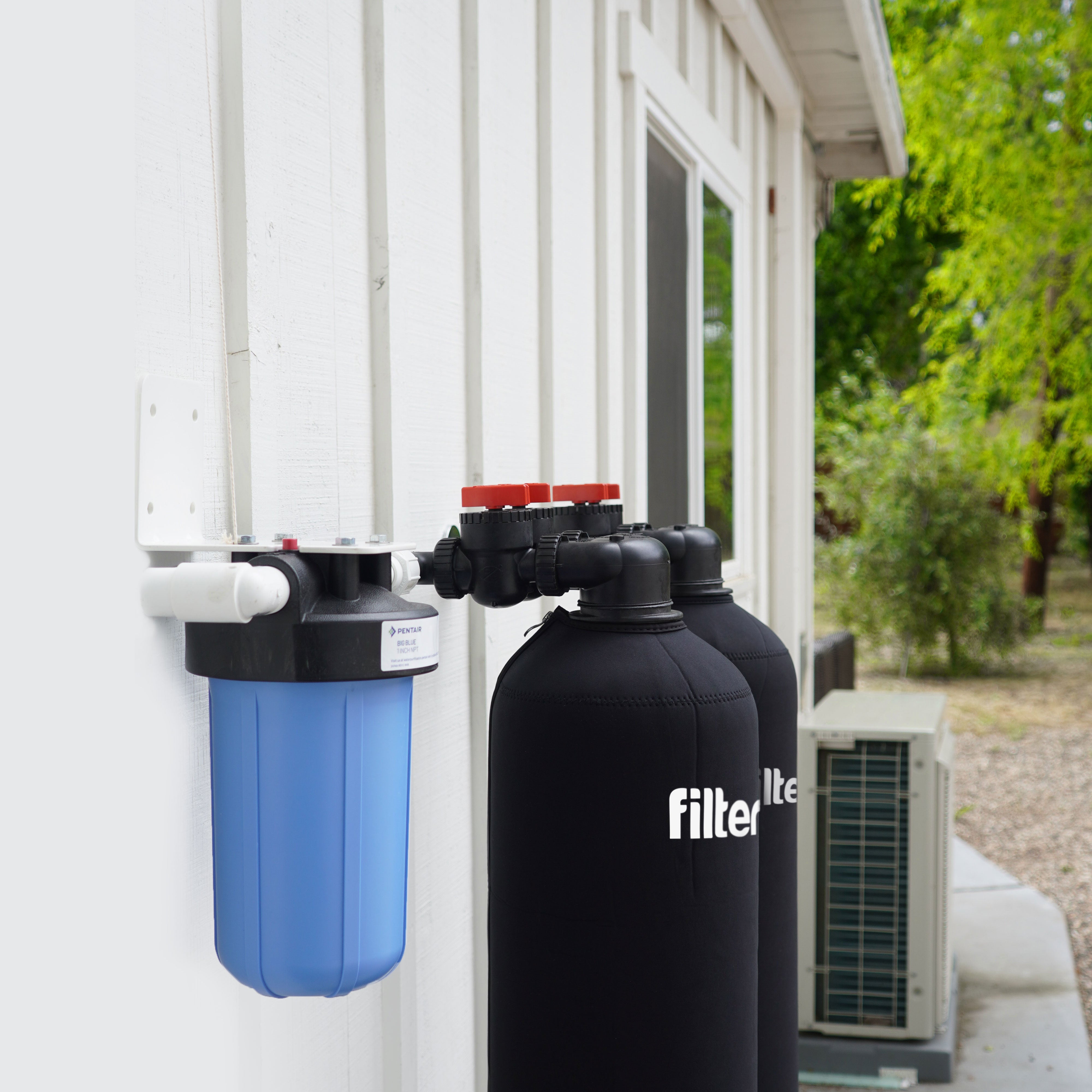 Outdoor water filtration system attached to a white wall.