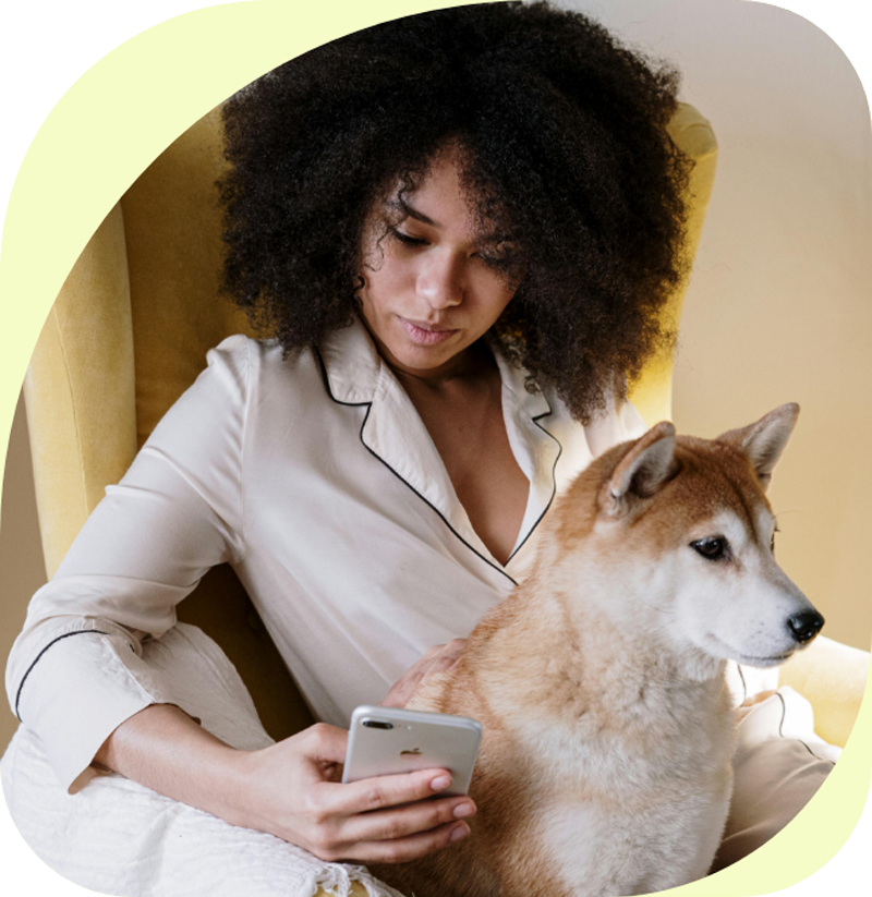 Person sitting with a dog, looking at a smartphone.