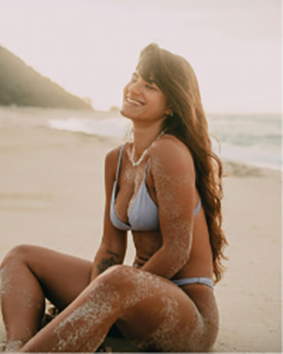 Smiling woman in a bikini sitting on a sandy beach.