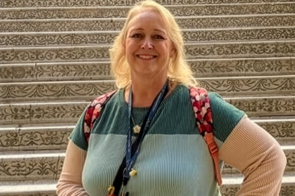 A smiling woman with short, curly brown hair, wearing a black and white striped top.