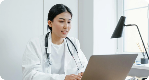 A doctor in a white coat using a laptop at a desk.
