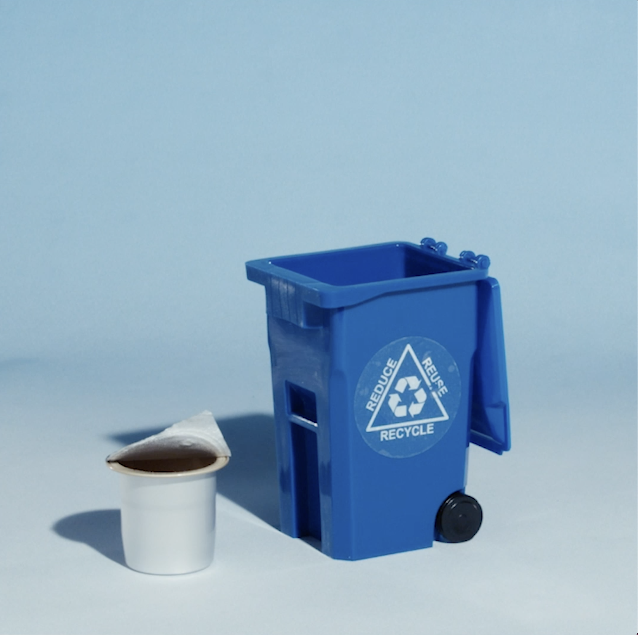 Small blue recycling bin next to a white cup with a lid.