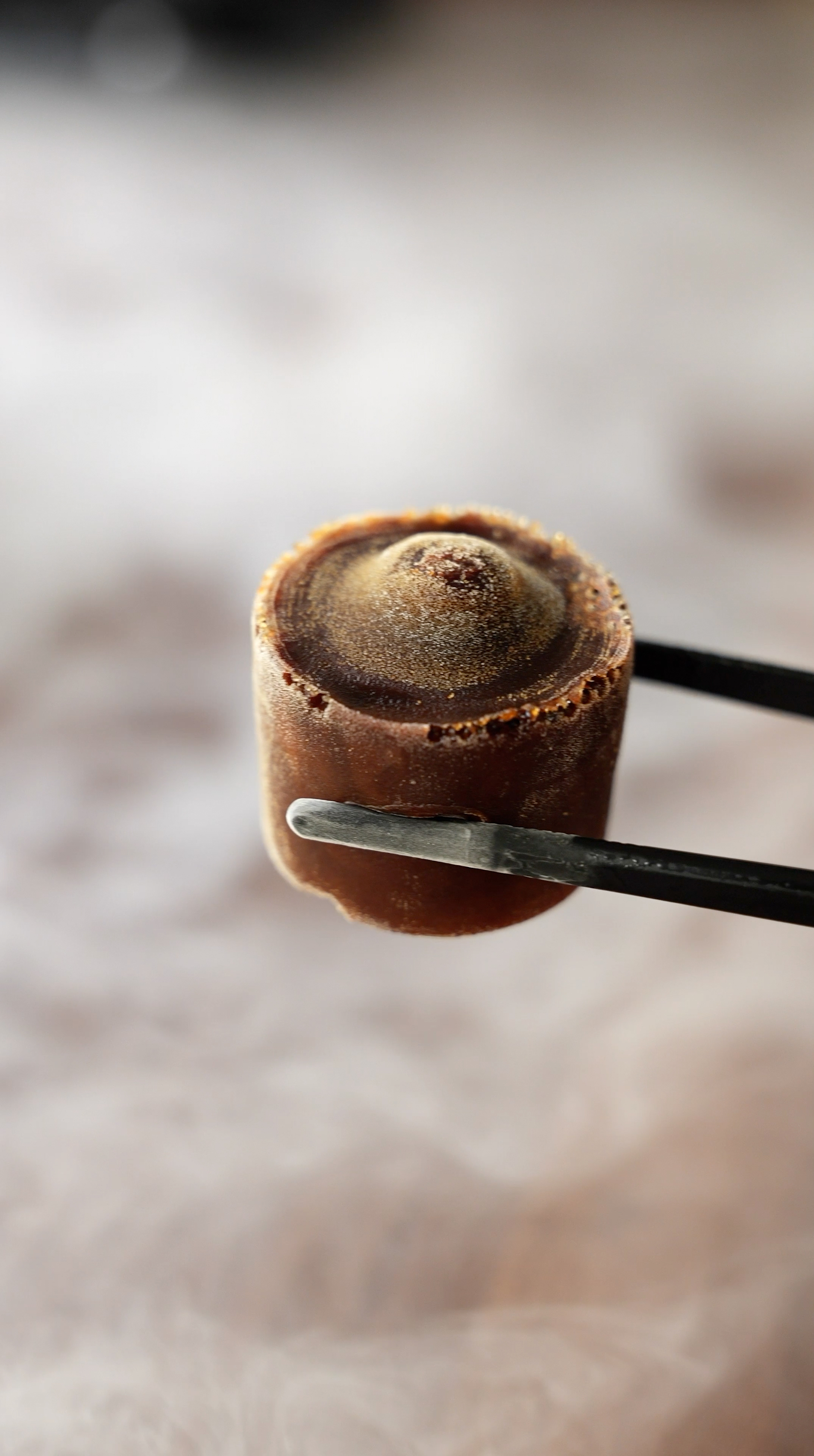 Close-up of a frozen brown dessert held by tongs.