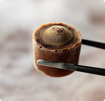 Close-up of a frozen chocolate dessert held by metal tongs.
