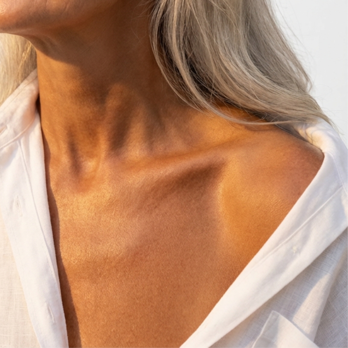 A close-up of a person's sunlit neck and collarbone in an open-collared white shirt.