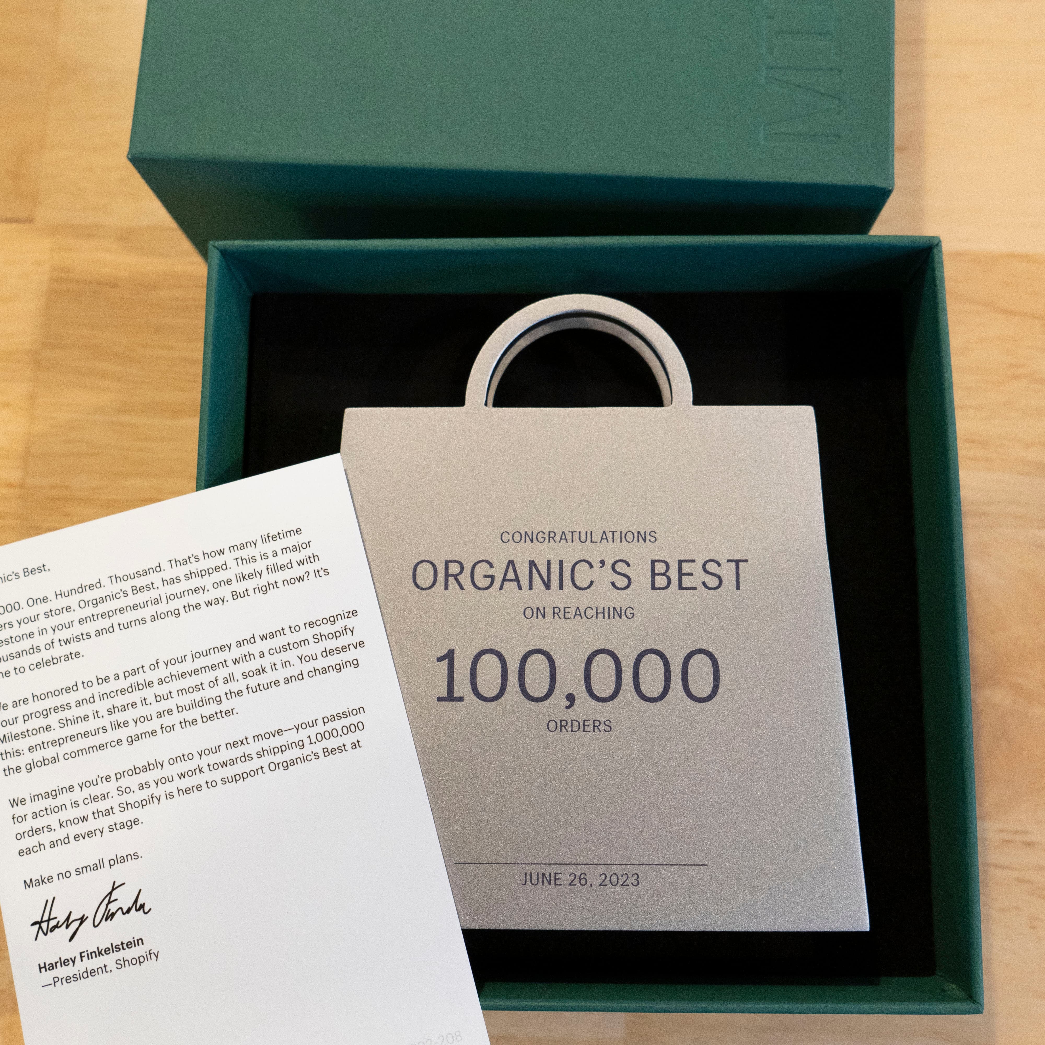 Plaque in a box congratulating Organic's Best on 100,000 orders, with a letter beside it.