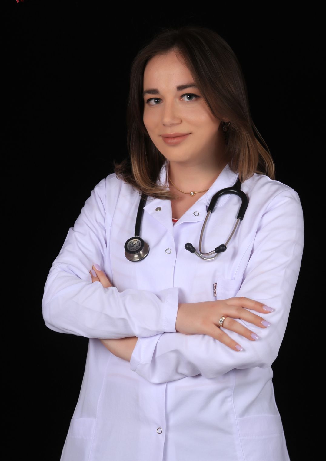 A woman in a white lab coat with a stethoscope around her neck poses with her arms crossed.