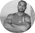 Man in a sleeveless shirt with arms crossed, standing outdoors.