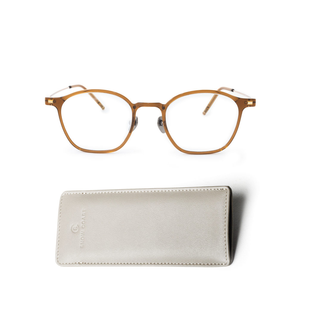 A pair of brown, round-framed eyeglasses sits above a light gray case on a white background.