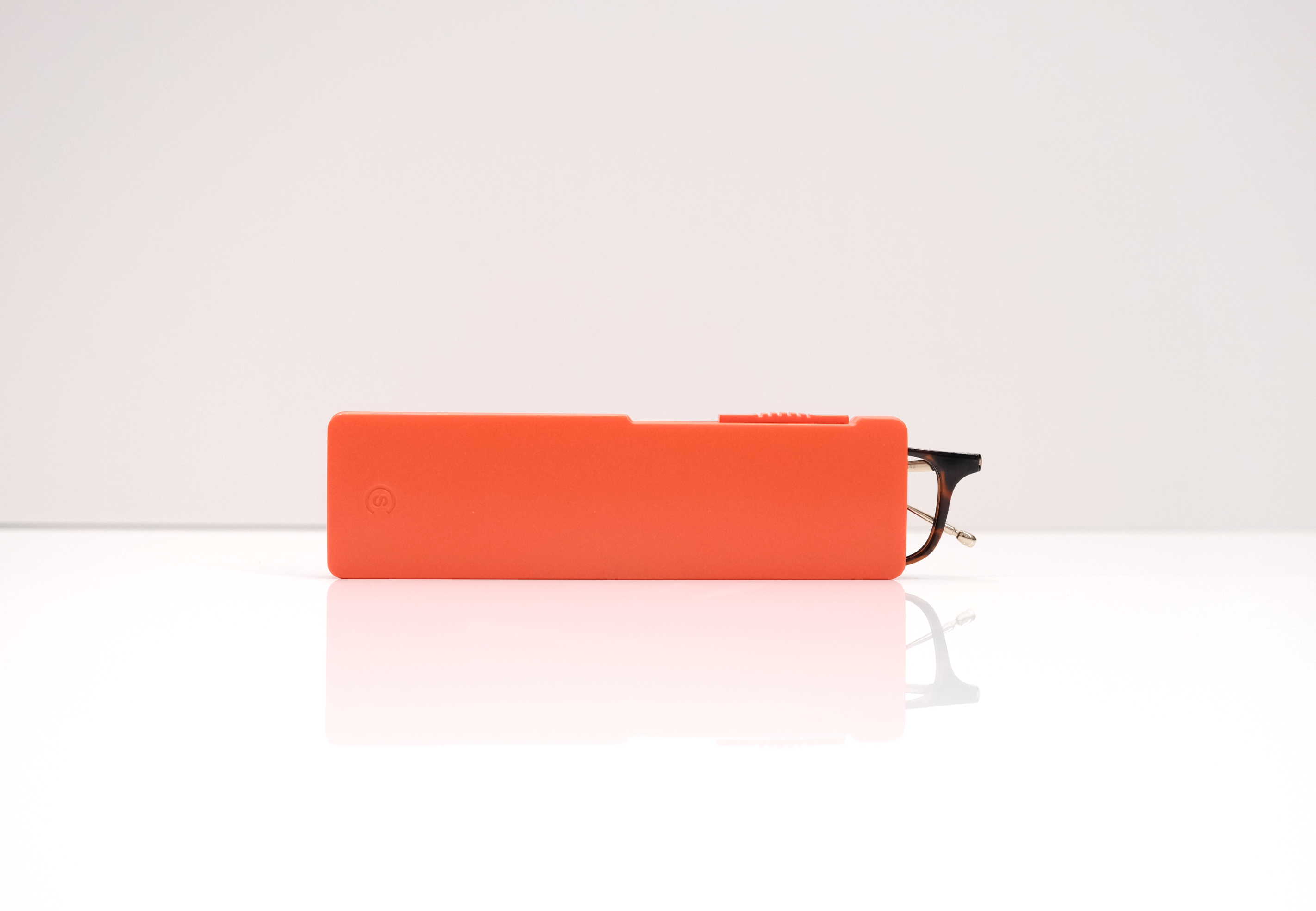 A pair of glasses sticking out of a bright orange case on a reflective white surface.