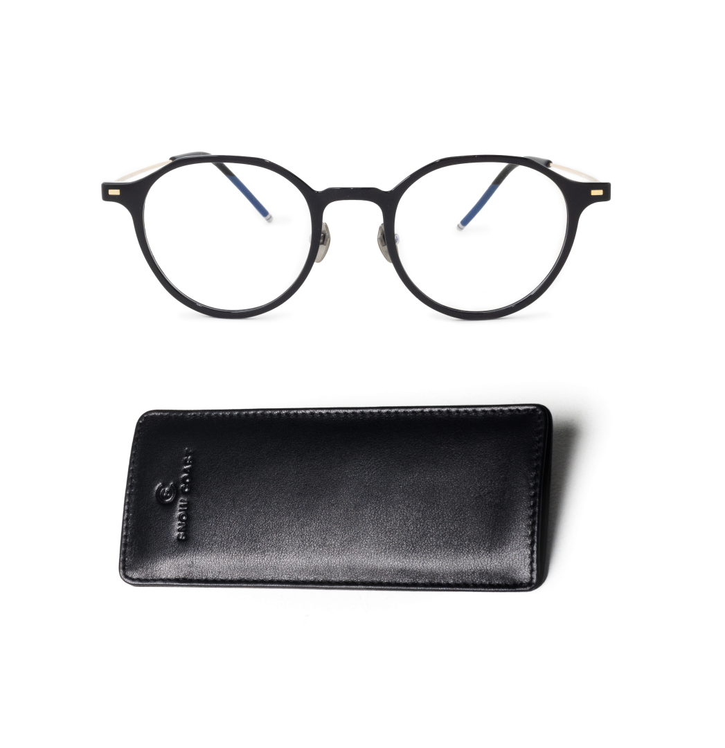 A pair of round, black-framed eyeglasses sits above a black leather case on a white background.