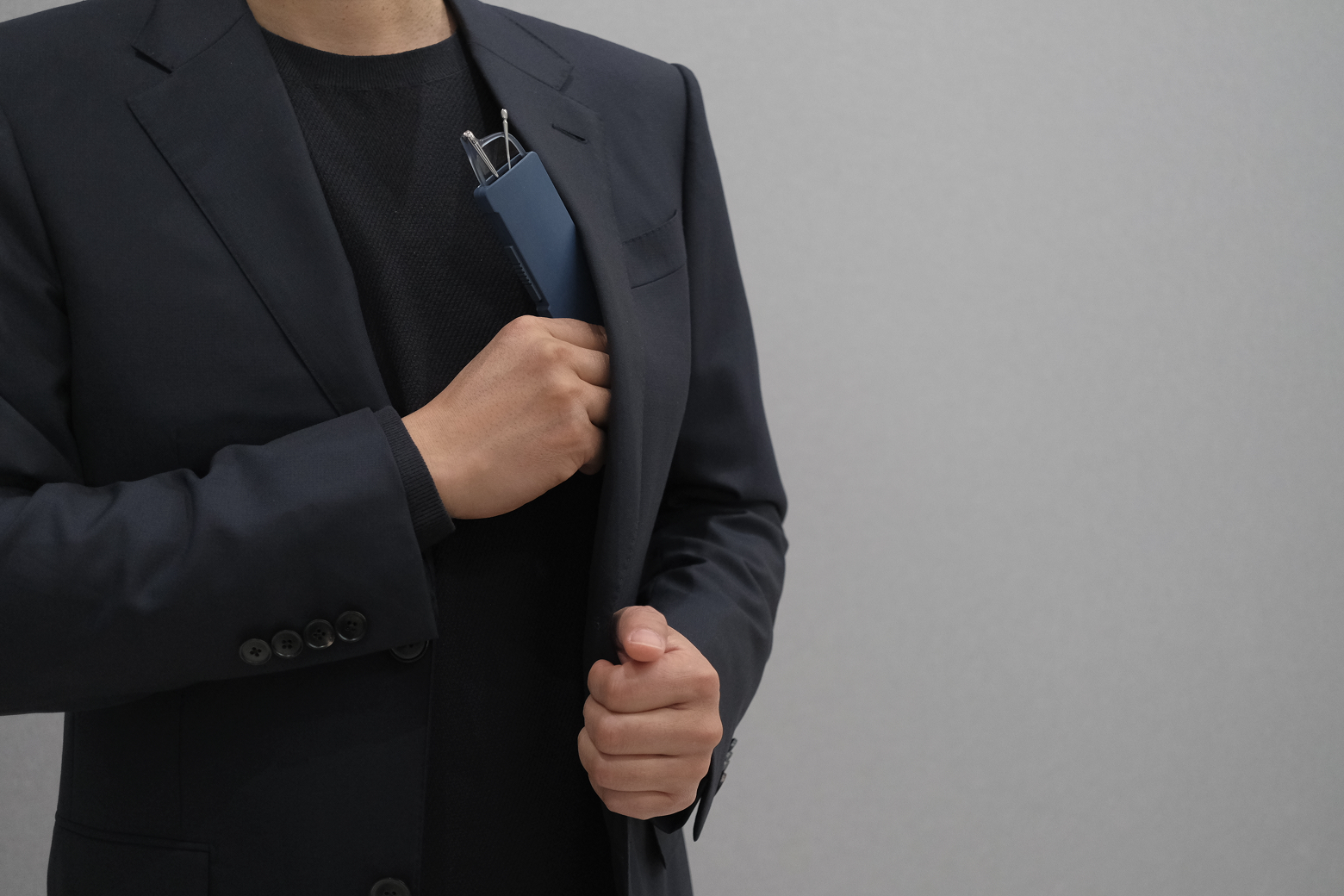 Man in a professional navy suit demonstrating the compact portability of the navy blue glasses case in a jacket pocket.