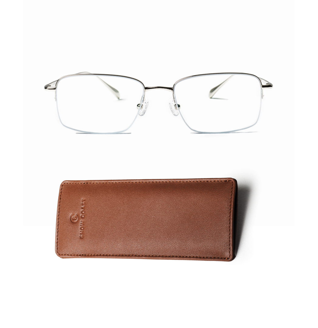 A pair of silver half-rimmed eyeglasses positioned above a brown leather case on a white background.