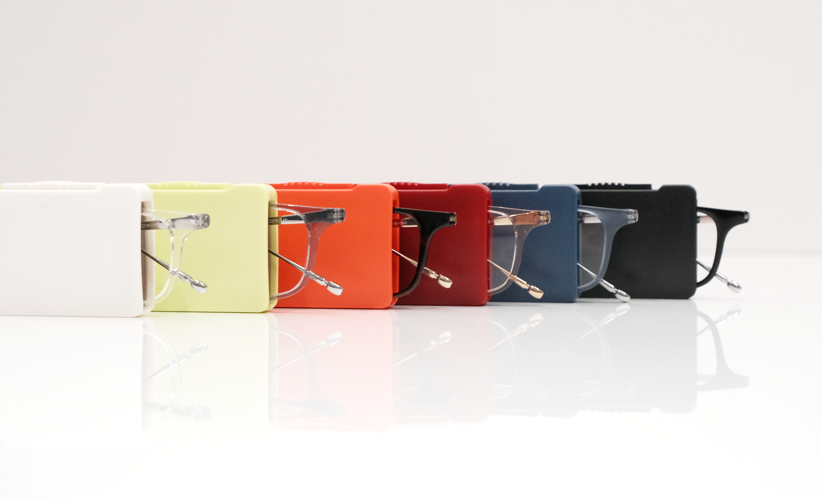 A row of eyeglasses in different colored cases on a reflective white surface.