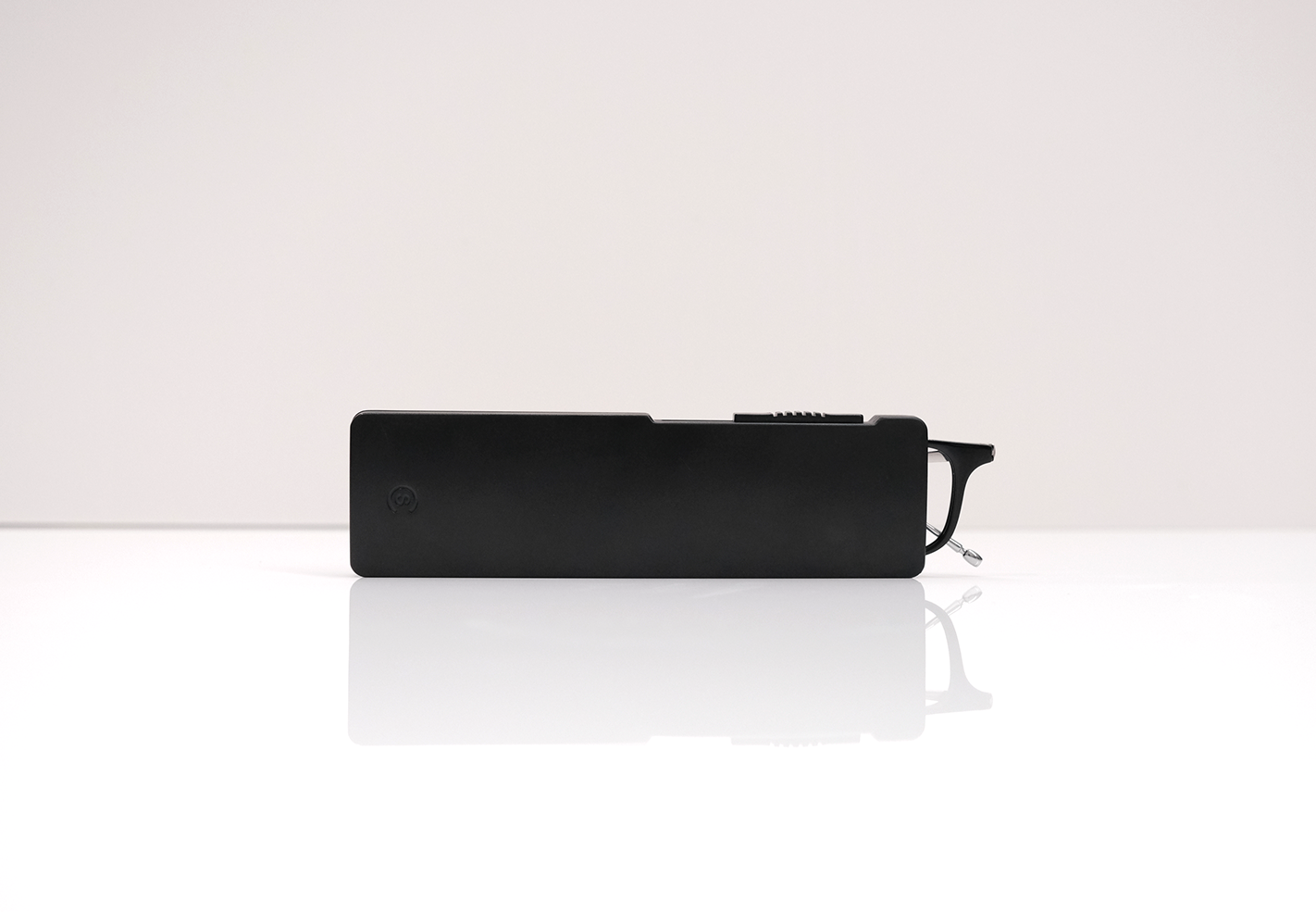 Side profile of the ultra-thin black glasses case on a reflective white surface, showcasing its minimal thickness.