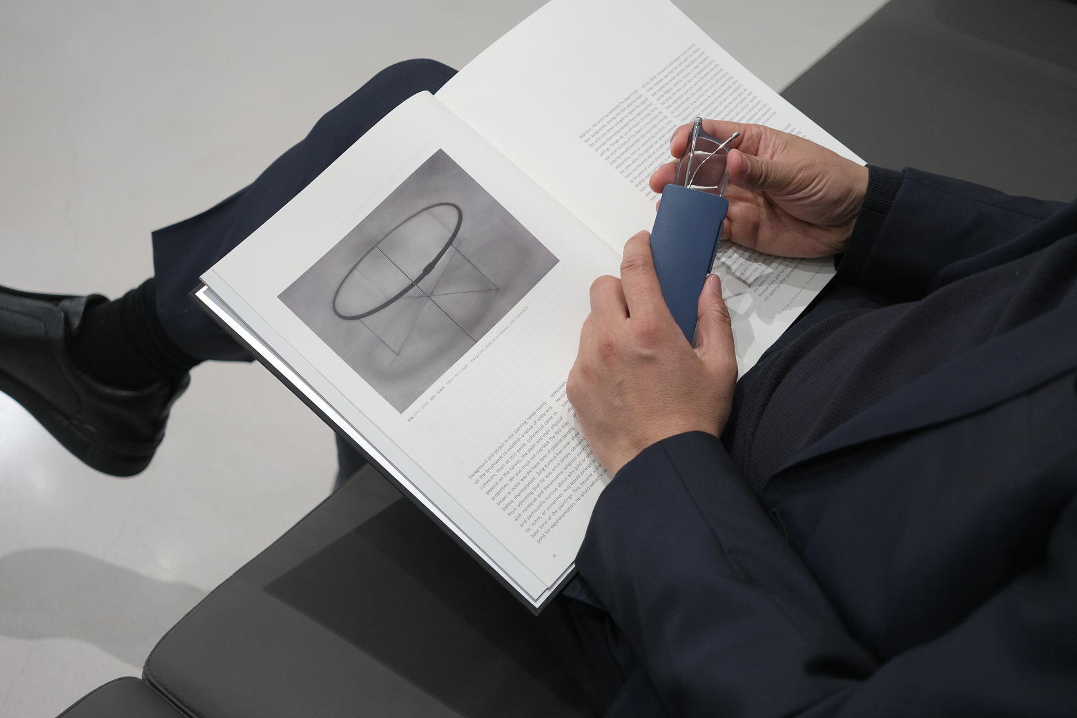 Close-up of a user placing clear-frame reading glasses into a slim matte blue case during a reading session.