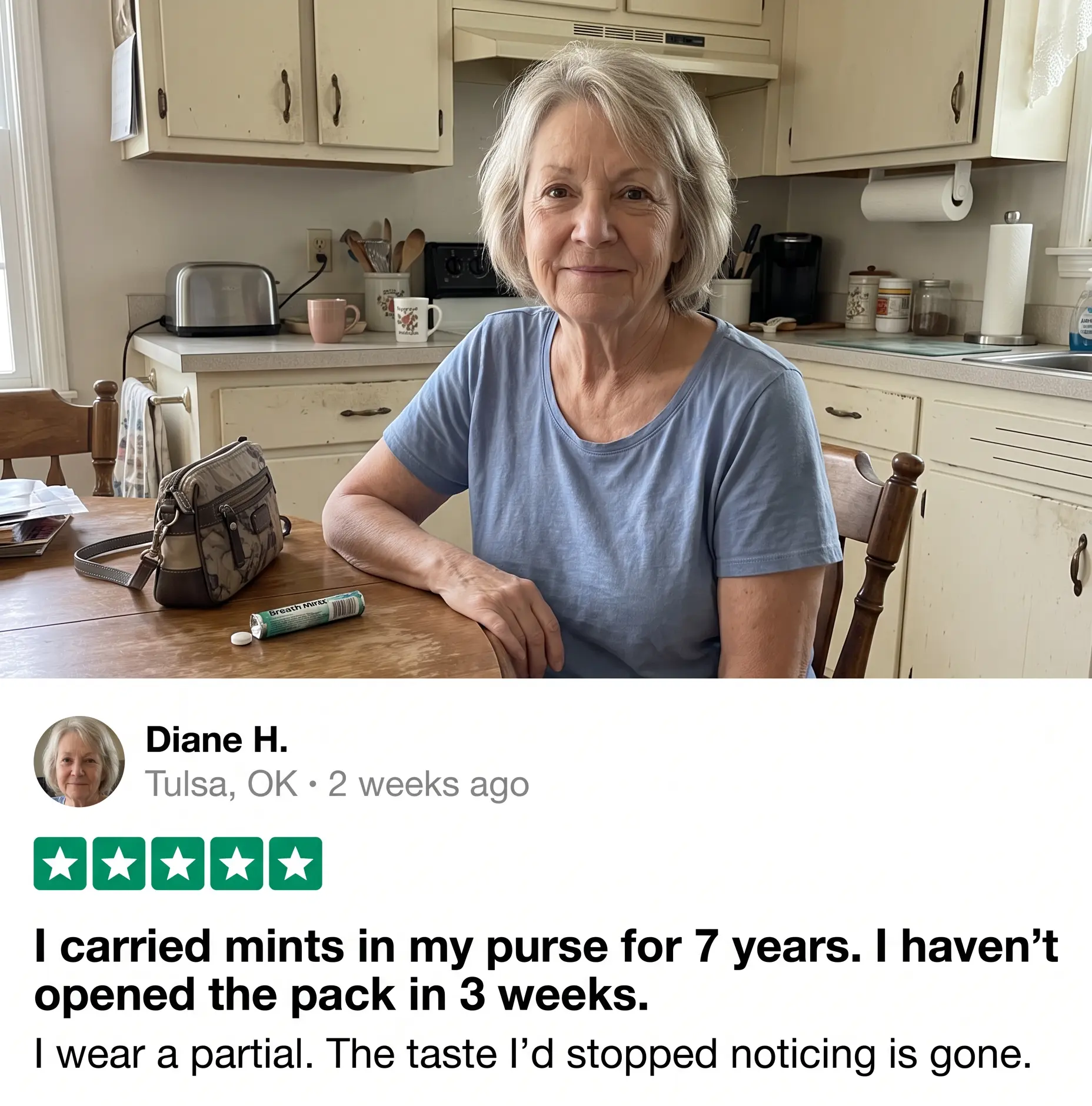 A woman in a blue shirt sits at a kitchen table with mints and a purse on it.