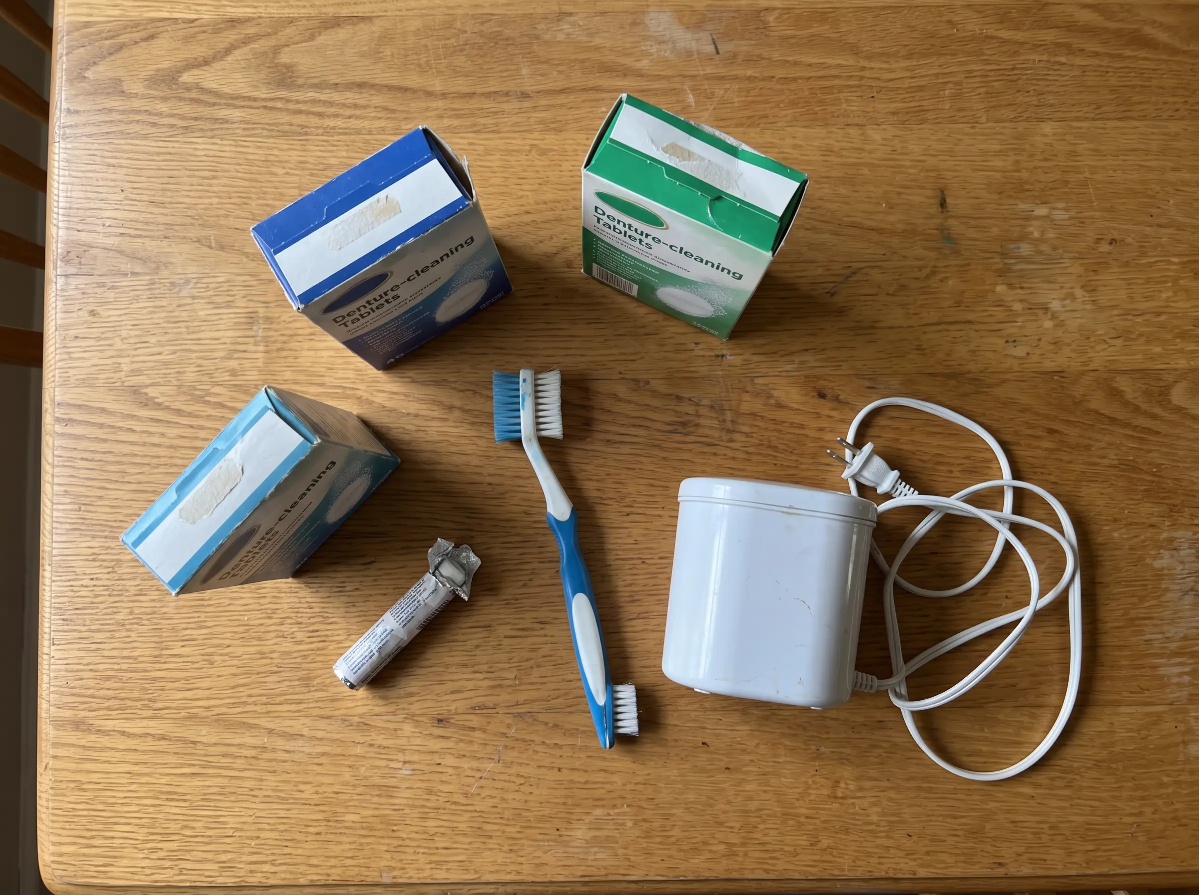 Denture cleaning supplies including tablets, a brush, and an electric cleaner on a wooden table.