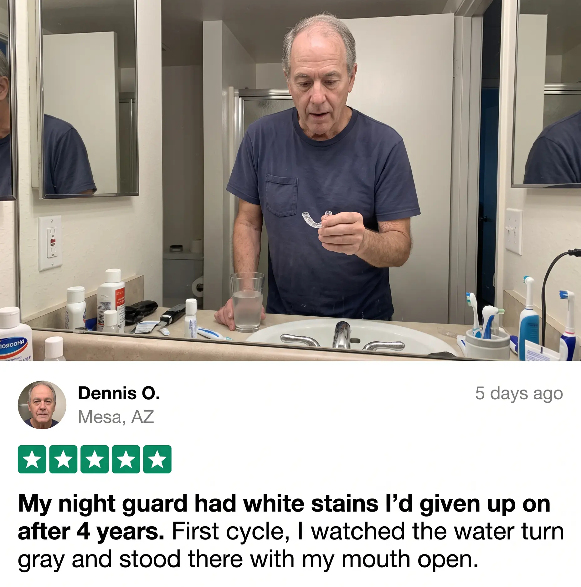 A man in a bathroom holds a clear dental night guard while looking at it.