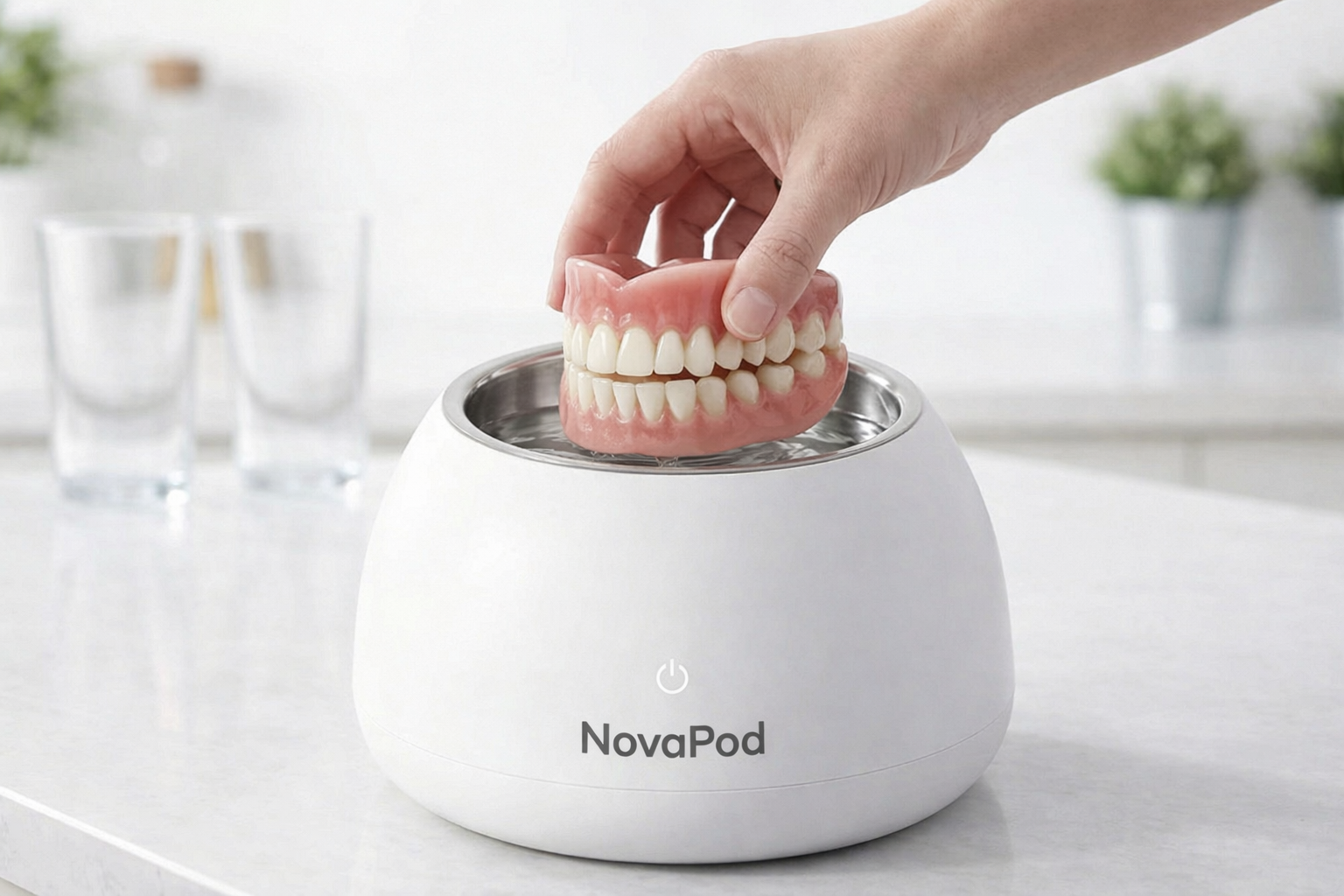 A hand lowers a full set of dentures into a white NovaPod denture cleaning device.