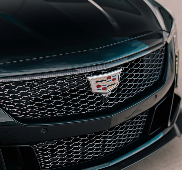A close-up shot of the front grille and emblem of a dark green Cadillac.