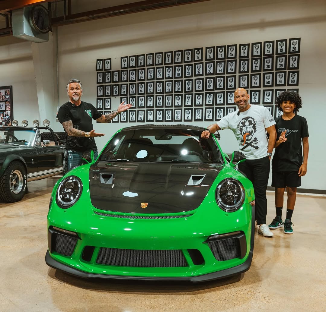 Three people posing with a green sports car in a garage.