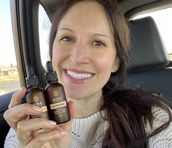 A woman sits in a car, smiling and holding up two brown dropper bottles from Aura Naturals.