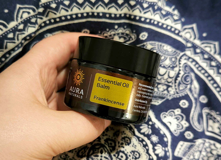 Hand holding a jar of Aura Naturals Essential Oil Balm, Frankincense flavor.