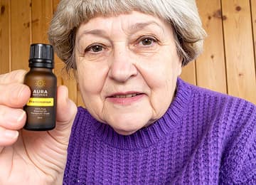 Person holding a small bottle, wearing a purple sweater, wooden wall background.