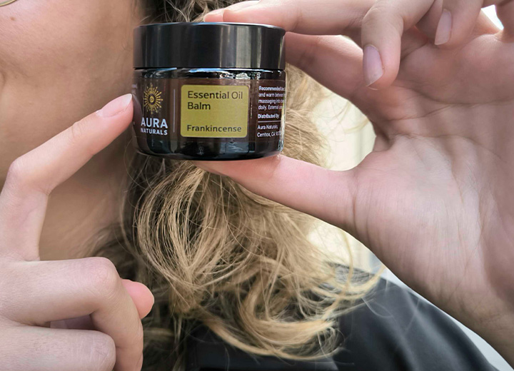 Person holding a jar of Aura Naturals Essential Oil Balm.