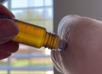 A hand applying oil to an elbow with a roller bottle.