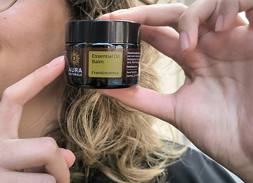 Person holding a jar of essential oil balm labeled 'Frankincense.'