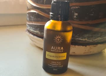 A bottle of Aura Naturals Frankincense essential oil on a table.