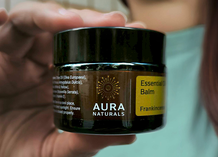 Hand holding a jar of Aura Naturals Essential Oil Balm.