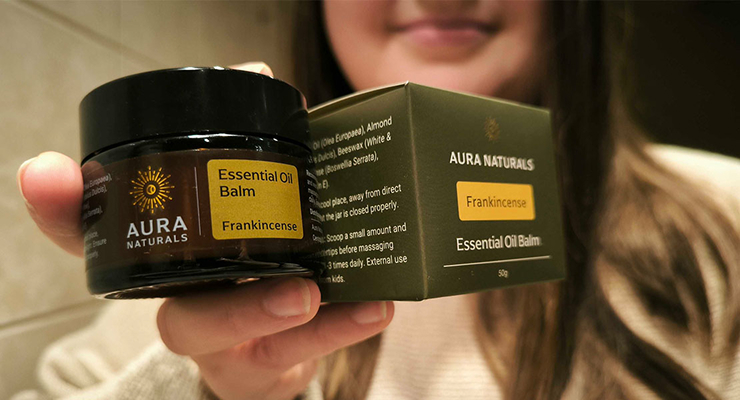 Person holding Aura Naturals Frankincense essential oil balm and its packaging.