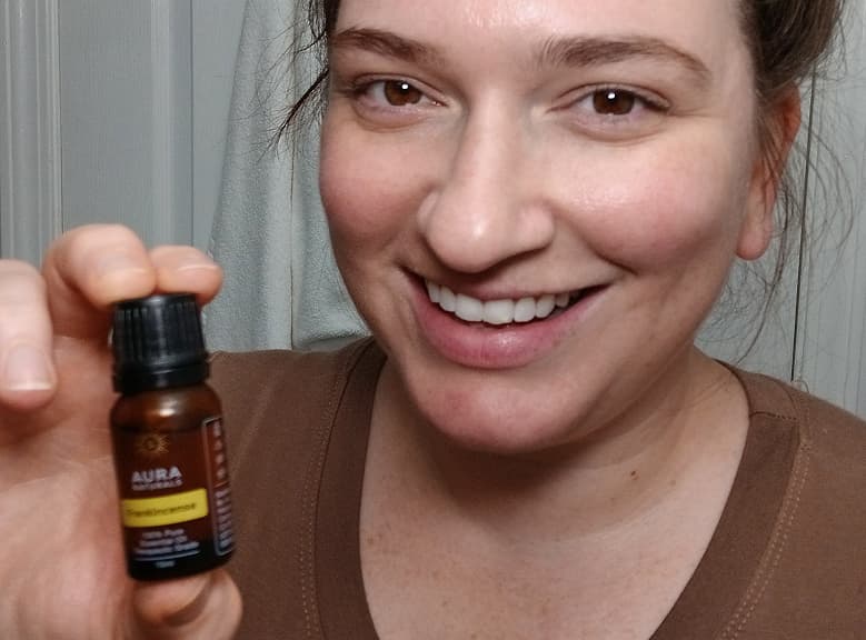 Person smiling and holding a small bottle labeled 'Aura Cacia Frankincense.'