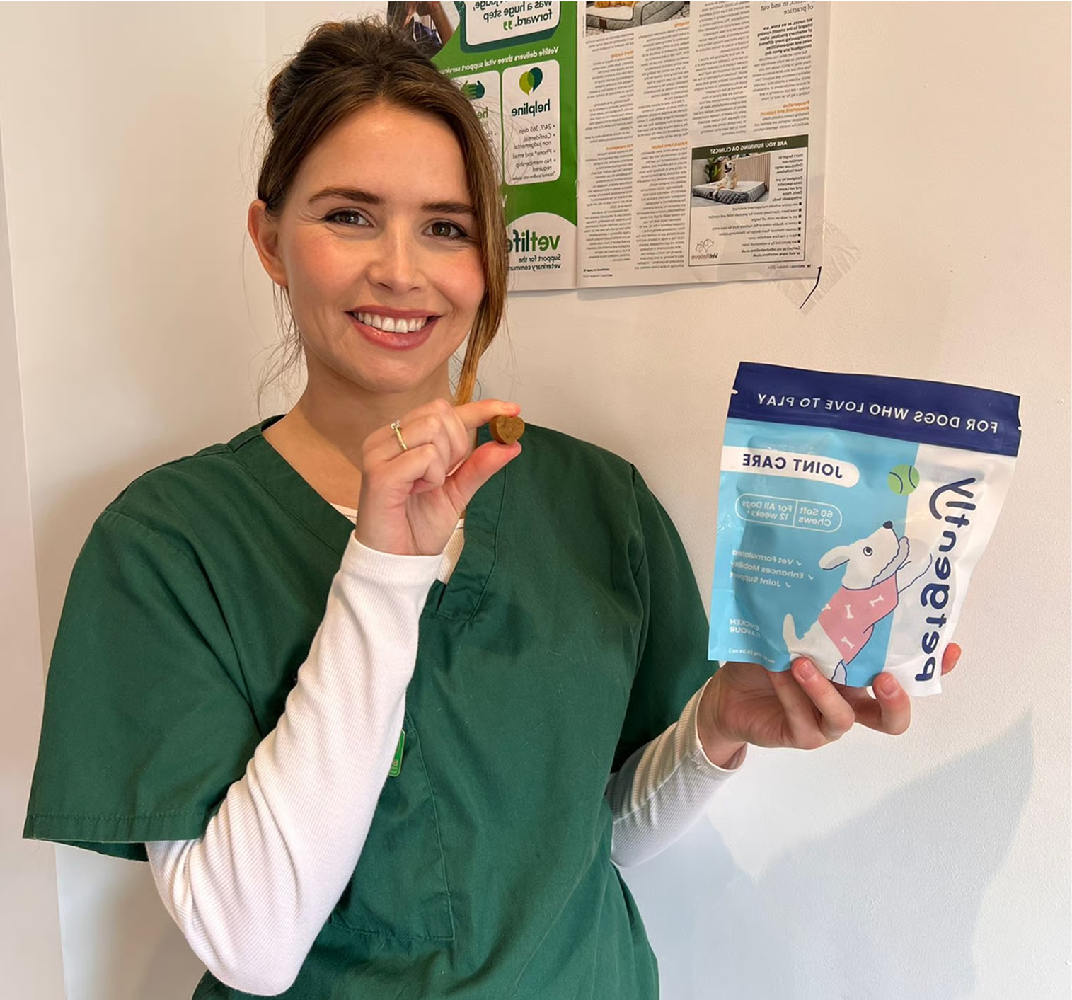 Person in green scrubs holding pet treat and package.