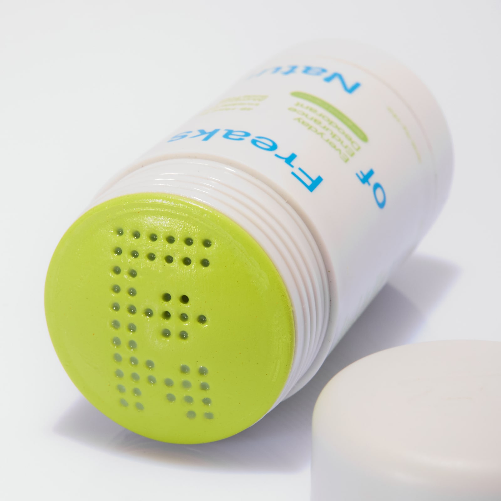 A white bottle with a perforated green cap lying sideways.