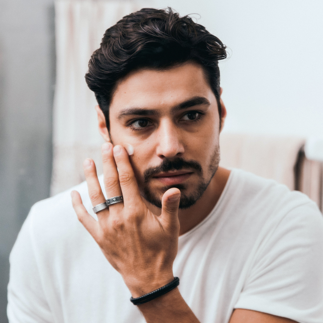 Man applying cream to his face, wearing a white shirt.