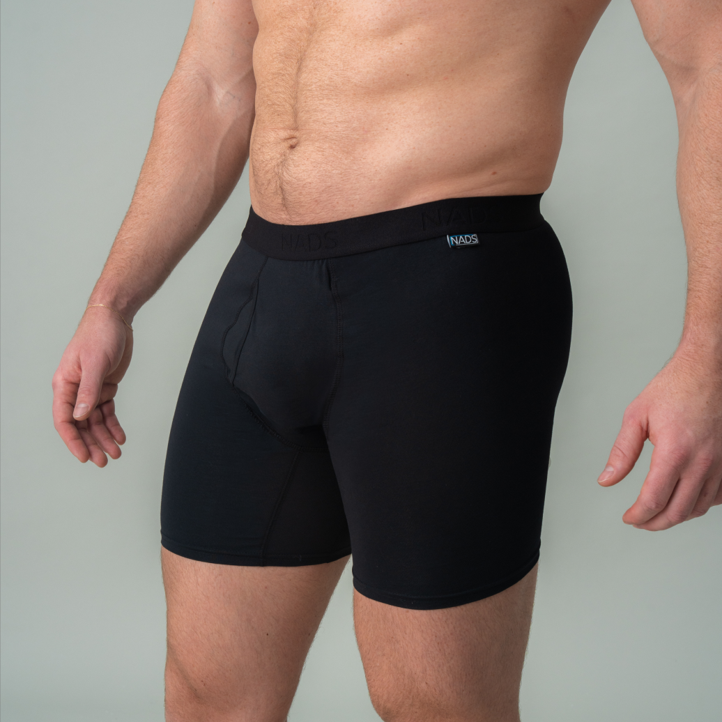 A man from the waist to mid-thigh wearing black boxer briefs against a grey background.