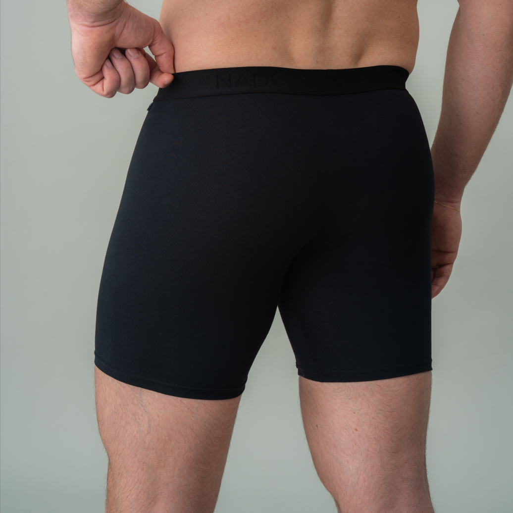 A man's back, shown from the waist down, wearing black boxer briefs and adjusting the waistband.