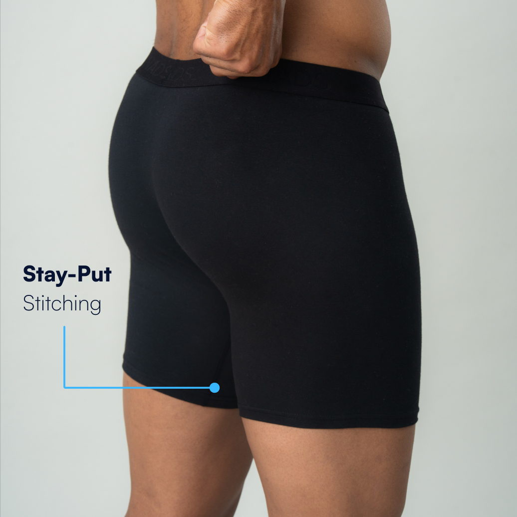 A side view of a man wearing black boxer briefs, with text highlighting the stay-put stitching on the thigh.