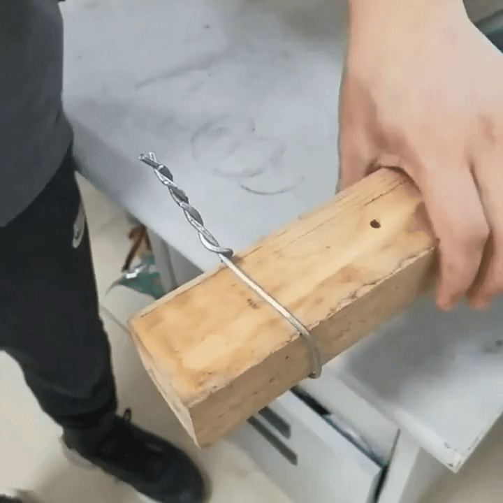 Hand holding a wooden block with a twisted wire hook.