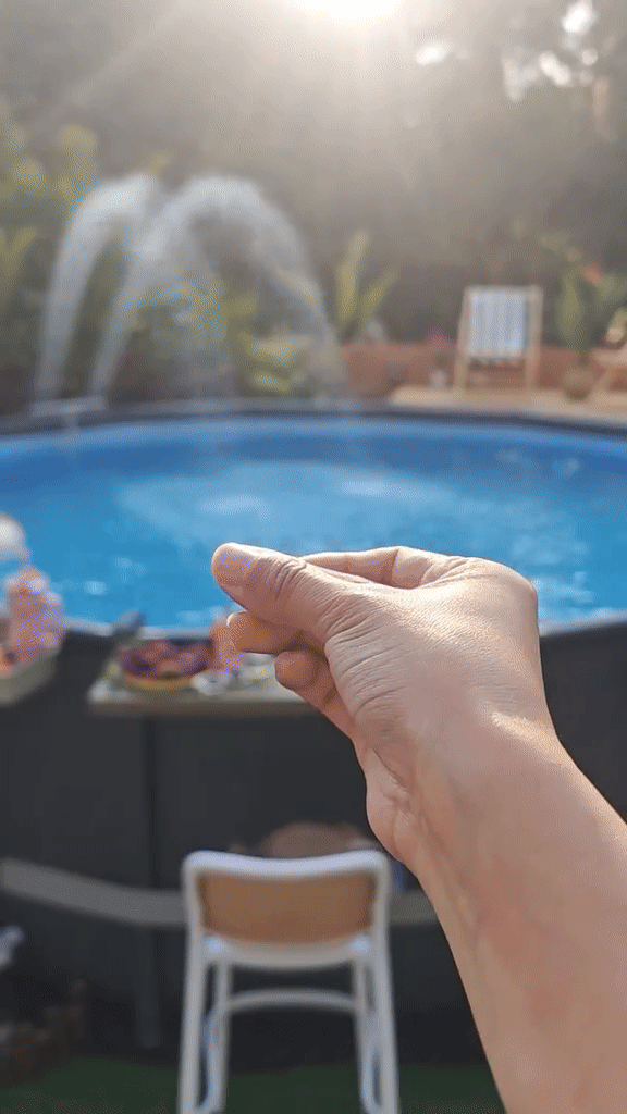 Hand with fingers pinched in front of a backyard pool.