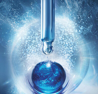 A close-up of a glass dropper dispensing a clear liquid onto a blue sphere surrounded by water bubbles.